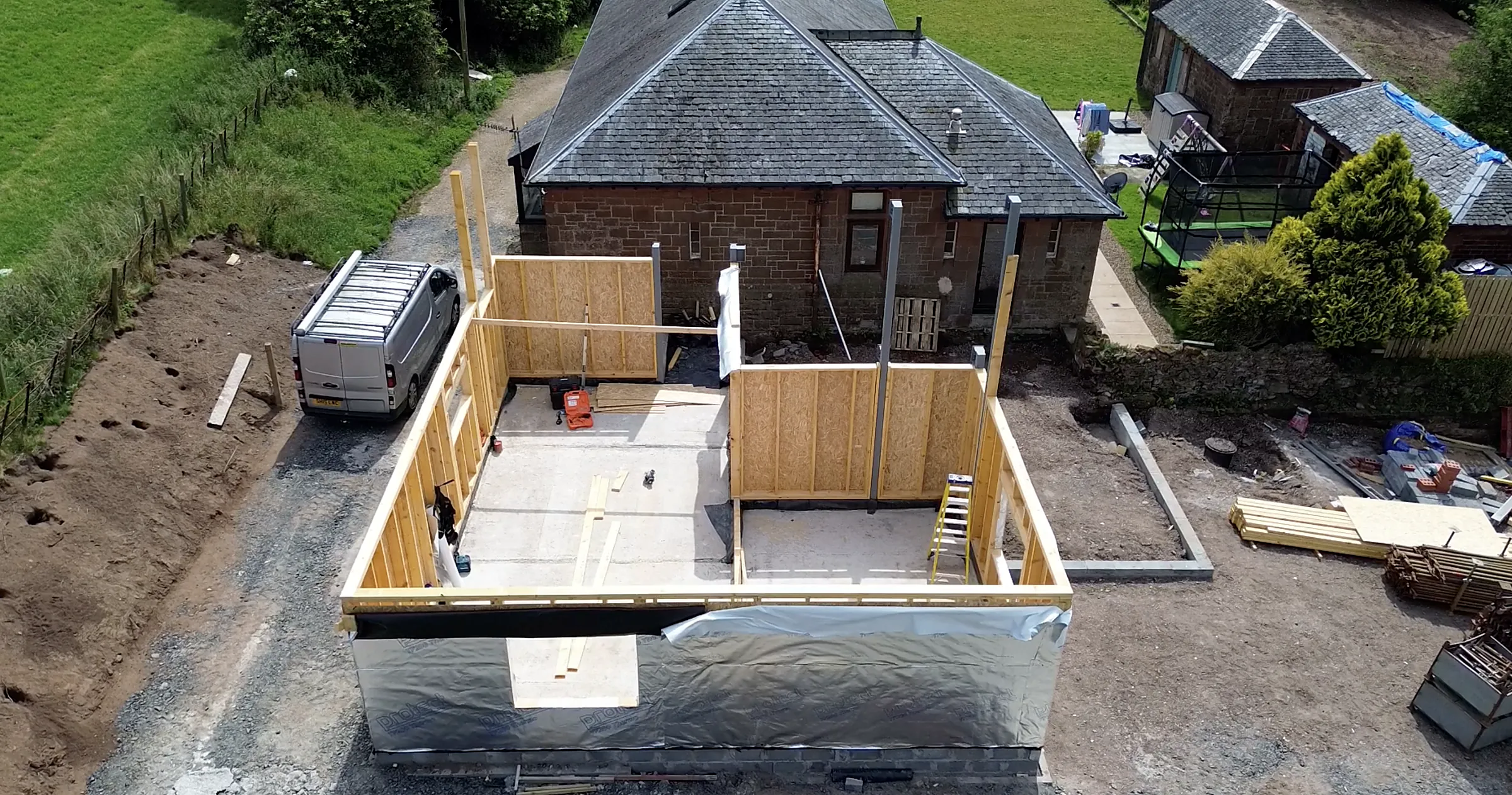 Aerial view of a timber frame extension going up beside a sandstone cottage
